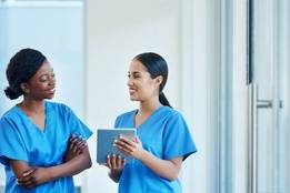 Two nurses in blue scrubs looking over charts