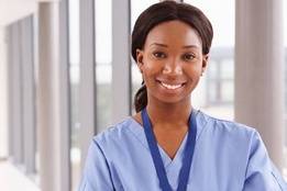 Nurse in blue scrubs smiling and standing in hospital hallway